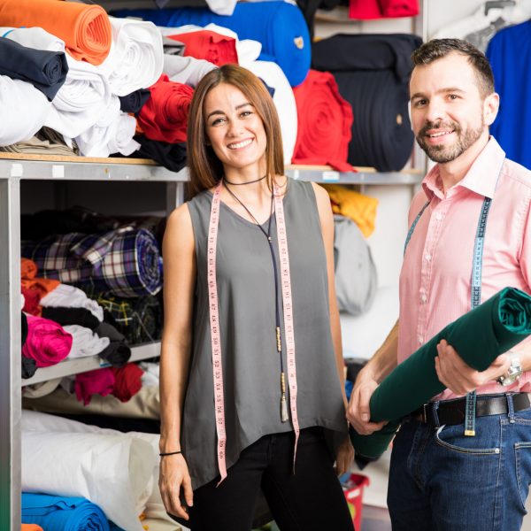 Portrait of a couple of successful Hispanic fashion designers looking at fabrics in a workshop